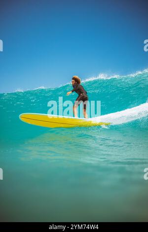 Un surfeur monte une planche de surf jaune sur une vague dans l'océan. Le surfeur porte une combinaison noire Banque D'Images