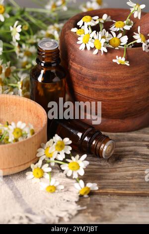 Bouteilles d'huile essentielle, fleurs de camomille, mortier et pilon sur table en bois Banque D'Images