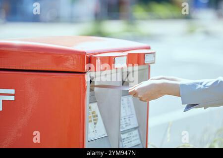 Main d'une jeune femme mettant une enveloppe dans une boîte aux lettres Banque D'Images