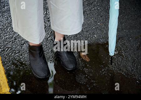 Pieds de femme avec imperméable et parapluie Banque D'Images