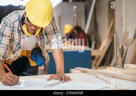 Menuisier dessinant des plans de table sur bois à un bureau de travail. constructeurs et ingénieurs concevant Banque D'Images