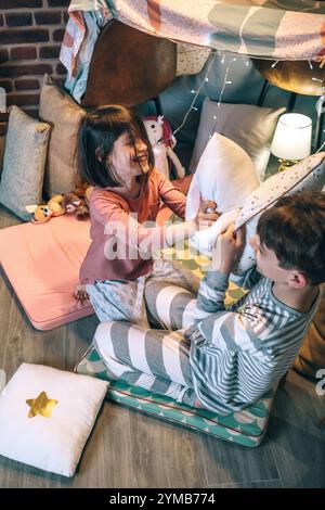 Garçon et fille excités riant dans la bataille de coussins sur le tipi diy dans la maison Banque D'Images