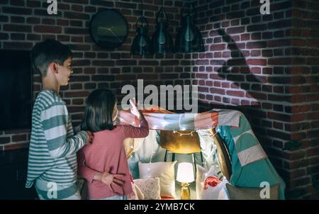Deux enfants en pyjama s'amusant à jouer avec des marionnettes d'ombre sur le mur de briques à la maison Banque D'Images
