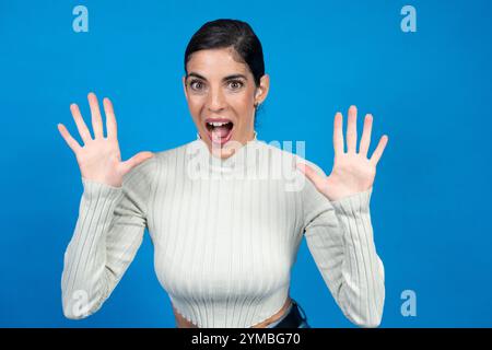 Femme brune montrant dix doigts avec les deux mains et criant sur un fond bleu Banque D'Images