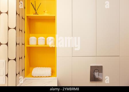 Gros plan d'étagères élégantes dans la salle de bain. Un accent lumineux sur la couleur jaune du mobilier. Intérieur moderne. Serviettes propres, bocaux, bâton parfumé Banque D'Images