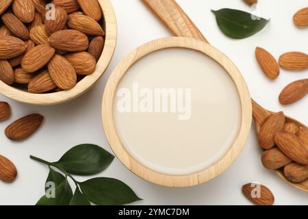 Lait de noix frais dans un bol, amandes et feuilles vertes sur une table blanche, pose à plat Banque D'Images