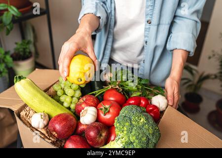 Déballage d'une boîte en carton contenant des fruits et légumes biologiques cultivés à la ferme à partir d'une commande en ligne. Épicerie en ligne. Banque D'Images