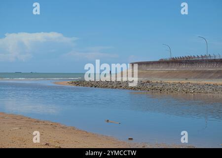 L'eau de mer recule autour de la plage et du barrage, et la silhouette d'une personne peut être vue au loin. Banque D'Images