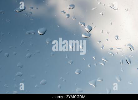 Gouttelettes d'eau claires dispersées sur une fenêtre en verre, réfléchissant la lumière et créant un motif texturé. Banque D'Images
