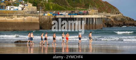 Une image panoramique d'un groupe de nageurs masculins en eau froide marchant dans la mer pour une baignade tôt le matin à Towan Beach à Newquay Cornwall Royaume-Uni. Banque D'Images