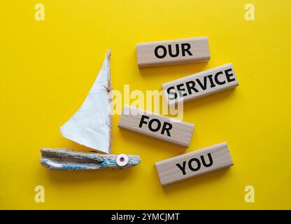 Notre service pour vous symbole. Blocs en bois avec des mots notre service pour vous. Beau fond jaune avec bateau. Affaires et notre service pour vous conc Banque D'Images