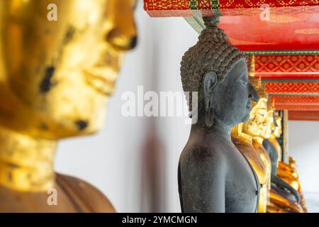 Bouddha noir dans une rangée de statues de Bouddha dorées dans le complexe du temple Wat Pho dans la ville de Bangkok, Thaïlande, Asie. Temple du Bouddha couché. Populaire Banque D'Images