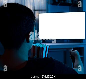 Gros plan d'un jeune homme regardant la télévision la nuit tout en mangeant du pop-corn dans son salon, concept de l'homme regardant la télévision Banque D'Images