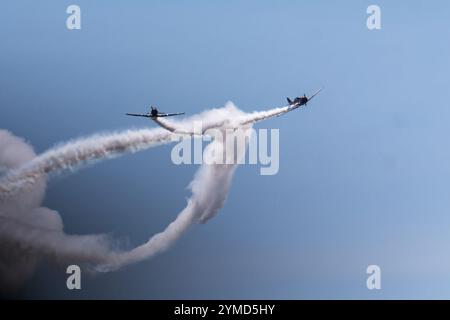 Deux avions vintage s'élèvent dans le ciel, traçant élégamment des motifs de fumée blanche sur un fond lumineux. Banque D'Images