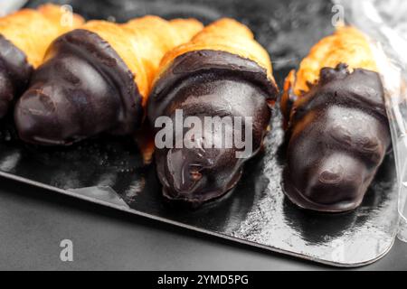 Gros plan de croissants enrobés de chocolat sur un plateau noir brillant. Délicieuses pâtisseries à la croûte dorée feuilletée et à la riche garniture sucrée foncée Banque D'Images