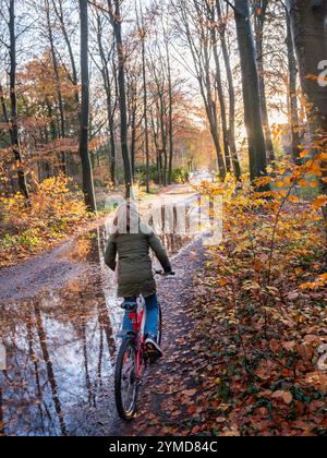 jeune fille sur le vélo sur le chemin forestier très humide passe des flaques en automne néerlandais près d'utrecht aux pays-bas Banque D'Images