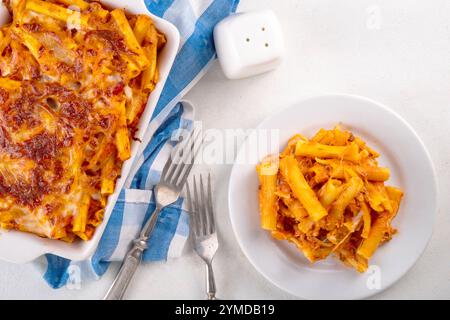 Pâtes Ziti cuites au four avec sauce tomate bolognaise ou marinara et fromage, dans une poêle et une assiette cuites, sur un espace de copie de table de cuisine blanc Banque D'Images