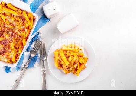 Pâtes Ziti cuites au four avec sauce tomate bolognaise ou marinara et fromage, dans une poêle et une assiette cuites, sur un espace de copie de table de cuisine blanc Banque D'Images