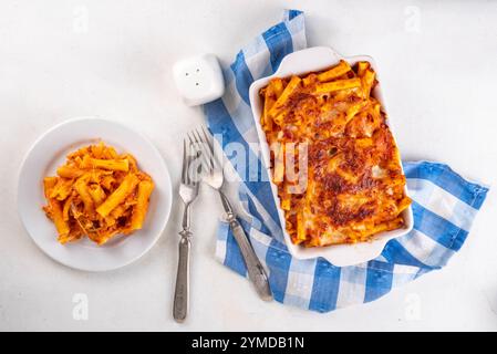 Pâtes Ziti cuites au four avec sauce tomate bolognaise ou marinara et fromage, dans une poêle et une assiette cuites, sur un espace de copie de table de cuisine blanc Banque D'Images