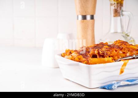 Pâtes Ziti cuites au four avec sauce tomate bolognaise ou marinara et fromage, dans une poêle et une assiette cuites, sur un espace de copie de table de cuisine blanc Banque D'Images