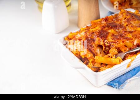 Pâtes Ziti cuites au four avec sauce tomate bolognaise ou marinara et fromage, dans une poêle et une assiette cuites, sur un espace de copie de table de cuisine blanc Banque D'Images