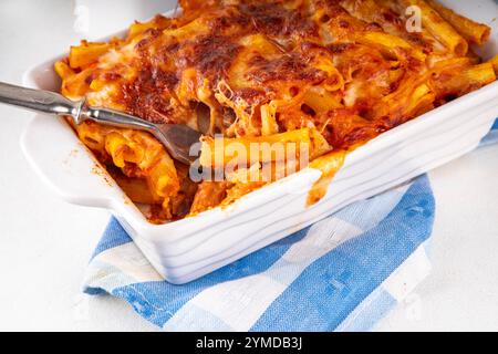 Pâtes Ziti cuites au four avec sauce tomate bolognaise ou marinara et fromage, dans une poêle et une assiette cuites, sur un espace de copie de table de cuisine blanc Banque D'Images