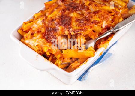 Pâtes Ziti cuites au four avec sauce tomate bolognaise ou marinara et fromage, dans une poêle et une assiette cuites, sur un espace de copie de table de cuisine blanc Banque D'Images