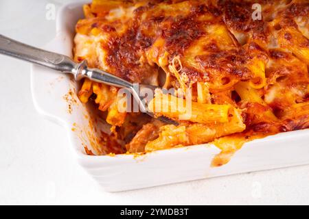 Pâtes Ziti cuites au four avec sauce tomate bolognaise ou marinara et fromage, dans une poêle et une assiette cuites, sur un espace de copie de table de cuisine blanc Banque D'Images