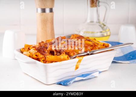 Pâtes Ziti cuites au four avec sauce tomate bolognaise ou marinara et fromage, dans une poêle et une assiette cuites, sur un espace de copie de table de cuisine blanc Banque D'Images