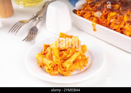 Pâtes Ziti cuites au four avec sauce tomate bolognaise ou marinara et fromage, dans une poêle et une assiette cuites, sur un espace de copie de table de cuisine blanc Banque D'Images