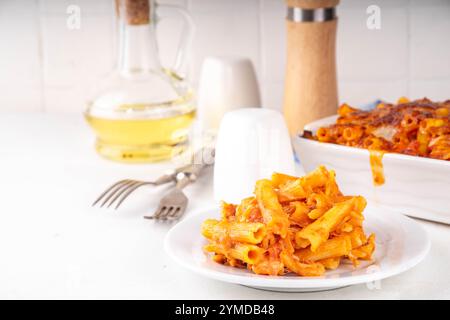 Pâtes Ziti cuites au four avec sauce tomate bolognaise ou marinara et fromage, dans une poêle et une assiette cuites, sur un espace de copie de table de cuisine blanc Banque D'Images