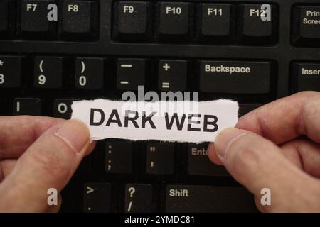 Un homme tenant un morceau de papier avec les mots Dark Web tapés dessus dans ses mains au-dessus d'un clavier d'ordinateur noir couvert de poussière. Gros plan. Banque D'Images