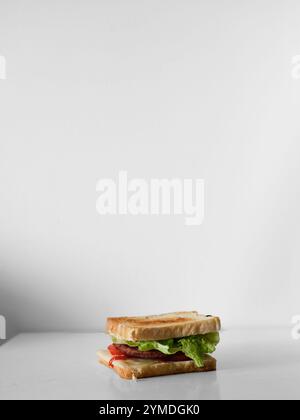 Un sandwich avec de la laitue et de la viande est sur une table blanche. Le sandwich est coupé en deux et placé sur la table Banque D'Images