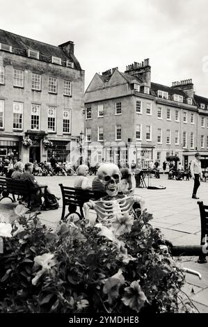 BATH, Royaume-Uni - 24 AOÛT 2017 : touristes, habitants et squelette drôle de détente à la place dans le centre de Bath en journée ensoleillée. Photo noir et blanc. Banque D'Images