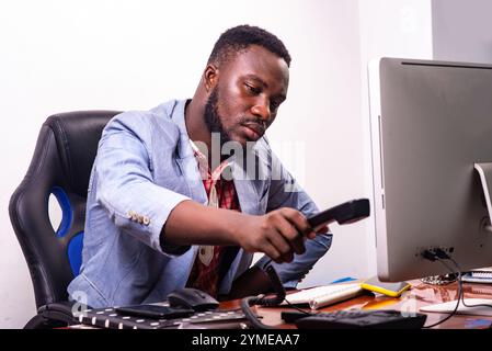 beau jeune homme d'affaires assis devant l'ordinateur portable dans le bureau ramasse ou pose le récepteur de téléphone. Banque D'Images