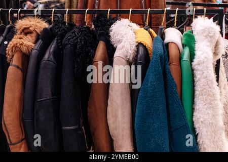 Détails de mode de manteaux de fourrure noir, marron, bleu moelleux, vêtements d'extérieur d'hiver suspendus dans une rangée sur des cintres dans une boutique de luxe de la mode Banque D'Images