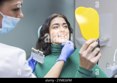 Femme dentiste, patiente tenant miroir. Tableau des nuances de dents Banque D'Images