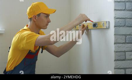 L'ouvrier dessine des marques sur le mur. Des lignes sont tracées pour la fixation Banque D'Images