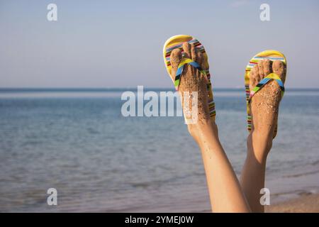 Jambes de femme sur fond de mer. Pieds en tongs. Pas de problèmes et d'agitation. Vacances de rêves Banque D'Images