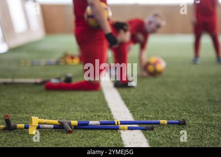 Des béquilles se trouvent sur l'herbe artificielle avec des joueurs de football handicapés en arrière-plan. Banque D'Images