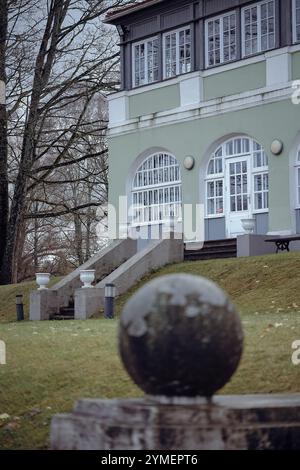 Un élégant bâtiment historique avec des fenêtres cintrées et des escaliers menant à un ornement sphérique en béton, entouré d'arbres et d'herbe par une journée nuageuse. Banque D'Images
