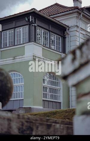 Un élégant bâtiment historique avec des fenêtres cintrées et des escaliers menant à un ornement sphérique en béton, entouré d'arbres et d'herbe par une journée nuageuse. Banque D'Images