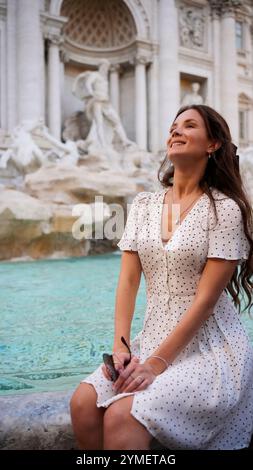 Femme souriante en robe à pois posant par Fontaine de Trevi à Rome, Italie Banque D'Images