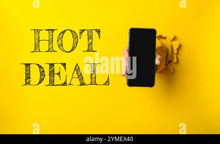 Personne tenant un téléphone avec le mot HOT DEAL écrit sur le mur derrière eux. L'image a une ambiance ludique et humoristique Banque D'Images