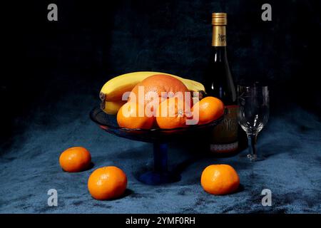 On y voit un vase avec une banane, des mandarines, une orange et une bouteille de vin de vigne dorée produit par l'usine Artemovsky dans la ville de Bakhmut. Banque D'Images