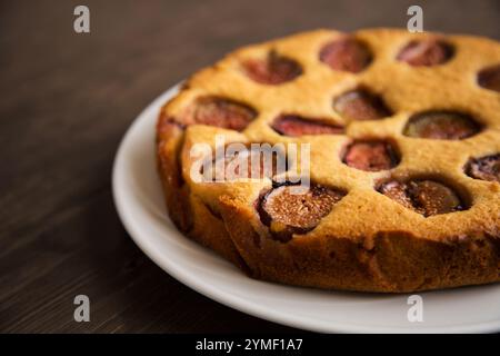 Gros plan d'une tarte aux figues fraîchement cuite sur une assiette blanche, présentant une croûte dorée et des tranches de figues juteuses sur un fond de table rustique en bois. Banque D'Images