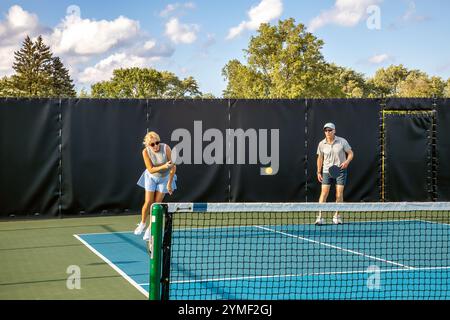 Une joueuse de pickleball retourne un tir alors que son partenaire masculin se tient à la ligne de base en attendant de retourner la balle. Banque D'Images