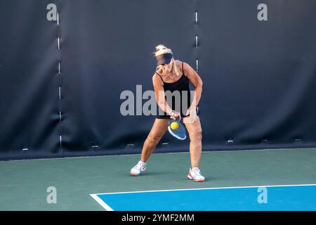 Une joueuse de pickleball retourne un service d'une balle jaune vif sur un terrain dédié dans un parc public. Banque D'Images