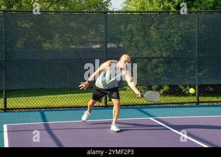 Un joueur de pickleball masculin retourne un service dans un terrain de pickleball violet et bleu dédié. Banque D'Images