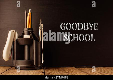 Un porte-crayon avec des crayons et un stylo se trouve sur un tableau noir avec les mots Goodbye School écrits en dessous Banque D'Images